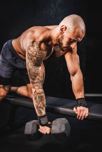 Знімок м'язової культурист робить важкі тренування з гантелі в спортзалі. Він накачує м'язи біцепсами з великою вагою
. - Фото, зображення