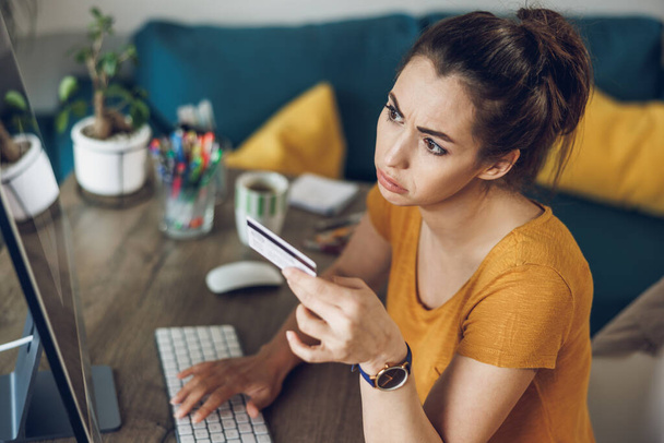 Młoda kobieta freelancer za pomocą karty kredytowej podczas pracy na komputerze w domu. - Zdjęcie, obraz