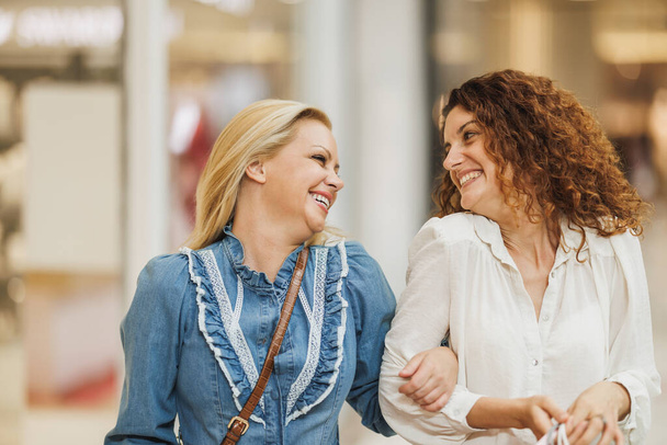 Retrato de uma alegre namoradas se unindo em um shopping ao fazer compras durante as vendas de Black Friday ou Cyber Monday. - Foto, Imagem