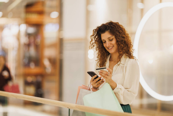Portrét šťastné ženy provádět platby kartou na její smartphone v nákupním centru během Černý pátek nebo kybernetické pondělí prodeje. - Fotografie, Obrázek