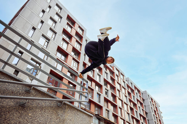 Гимнаст, спортсмен, молодой парень прыгает, перекидывается стеной, практикует паркур в общественном парке среди высотных зданий на рассвете. Концепция образа жизни, экстремального спорта, фристайла, деятельности, движения. Объявление - Фото, изображение
