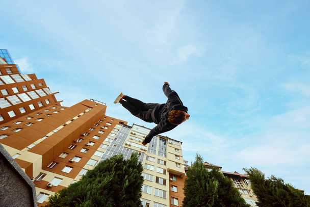 Atleet man, jongeman springen hoog, maken back-flip over stad, hoogbouw en uitzicht op de lucht in het openbaar park. Oogvisfilter. Concept van levensstijl, extreme vormen van sport, freestyle, activiteit. Steun - Foto, afbeelding