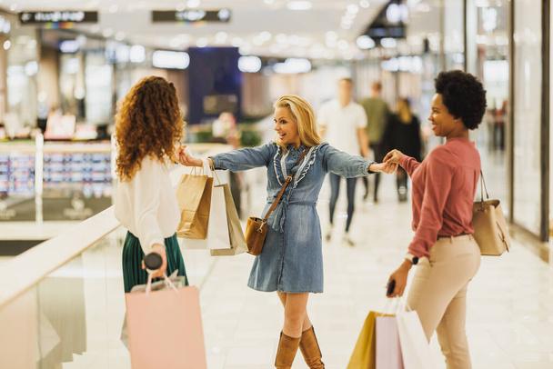 Girato di tre giovani donne attraenti divertirsi e in piedi in un centro commerciale insieme mentre fuori su una furia dello shopping. - Foto, immagini