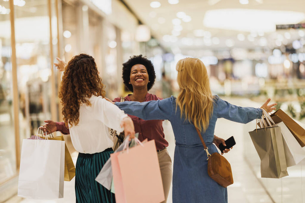 Красивая улыбающаяся Черная женщина обнимает своих лучших друзей в торговом центре во время воссоединения во время шоппинга. - Фото, изображение
