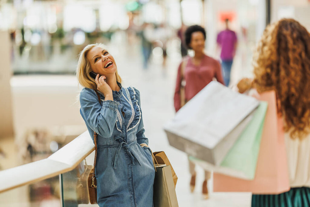 Wesoła kobieta zakupoholiczka rozmawiająca na smartfonie podczas zakupów w centrum handlowym podczas sprzedaży Black Friday lub Cyber Monday. - Zdjęcie, obraz
