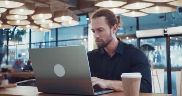 Távoli munka. Szabadúszó gyakorlat az irodán kívüli helyről történő munkavégzéshez, számítógép és internet kapcsolat a feladatokhoz. Szabadúszó férfi ül egy modern kávézó koncepció távoli munka laptop számítógép. - Felvétel, videó
