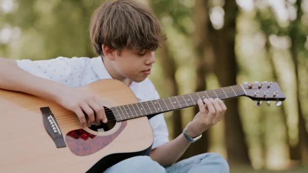 Кадри хлопчика-підлітка, який грає на акустичній гітарі в парку. - Кадри, відео