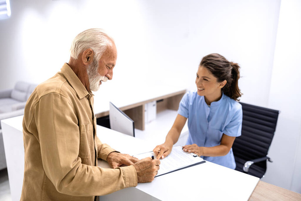 Enfermera ayudando al paciente mayor a llenar un cuestionario médico antes de visitar al médico en el hospital. - Foto, Imagen