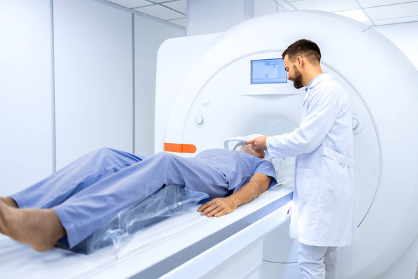 Радиолог или техник, готовящий старшего человека к полной МРТ или КТ головы в онкологическом диагностическом центре. - Фото, изображение