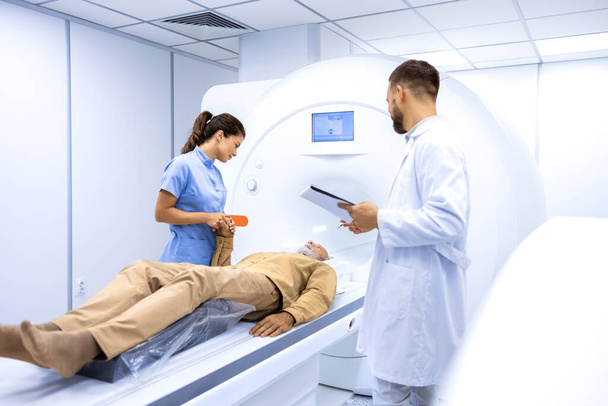 Experienced radiologists encouraging senior patient before MRI or CT scanning procedure in hospital. - Photo, Image