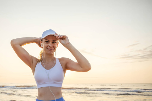 A girl of European appearance in a white cap stands against the background of the sea wearing headphones, there is a place for an inscription High quality photo - Photo, Image