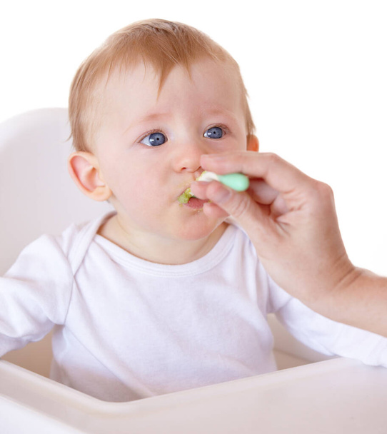 Niedlich, löffel und baby essen gemüse im fütterungsstuhl in einem studio für gesundheit und ernährung. Süß, natürlich und Junge neugeboren, Kind oder Kind genießen eine Mahlzeit für Wellness-Diät vor weißem Hintergrund - Foto, Bild