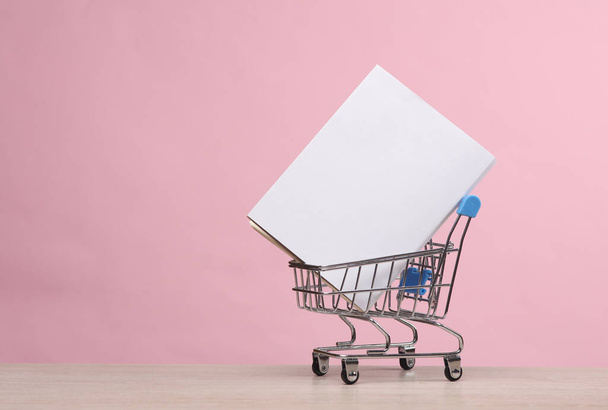 ピンクの背景に白いカバーの本のモックアップが付いている小型スーパーマーケットのカート - 写真・画像