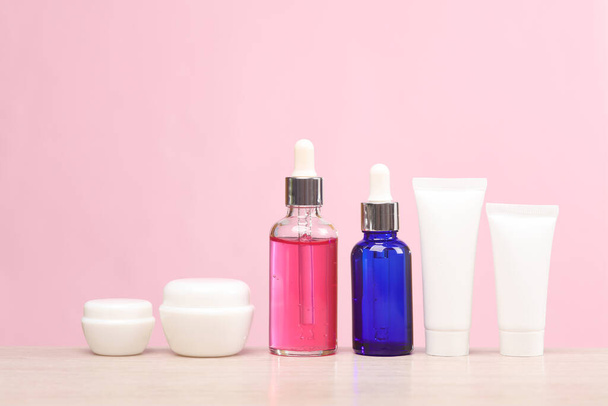 Arc szérum palackok, krém csövek és üvegek az asztalon, rózsaszín háttér. A bőregészség és az ifjúság fogalma - Fotó, kép