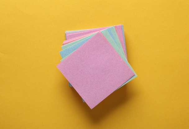 Stapel von farbigen quadratischen Notizblättern auf gelbem Hintergrund. Ansicht von oben - Foto, Bild