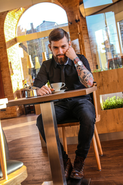 Hombre con tatuaje en brazos en una cafetería
 - Foto, imagen