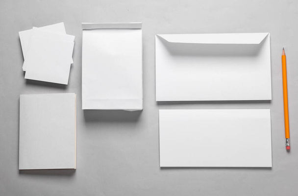 Макет з об'єктами офісу з білого паперу. Білий порожній конверт з листом, обідньою сумкою, візитною карткою, блокнотом та паперовими паперами на сірому фоні. Шаблон для дизайну. Вид зверху - Фото, зображення