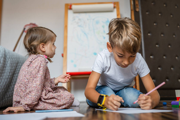 one small caucasian boy with sister child draw with crayon at home - Photo, Image