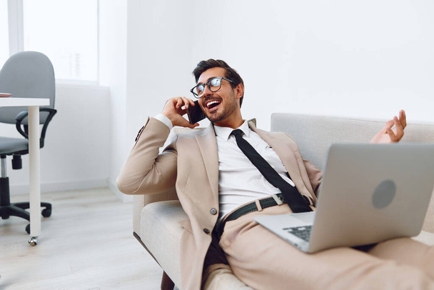 Emberek férfi győztes üzletember mosoly telefon mobil okostelefon talk szemüveg ruha telefon számítógép videó fiatal kanapé hívás iroda hívás vállalati laptop munka - Fotó, kép