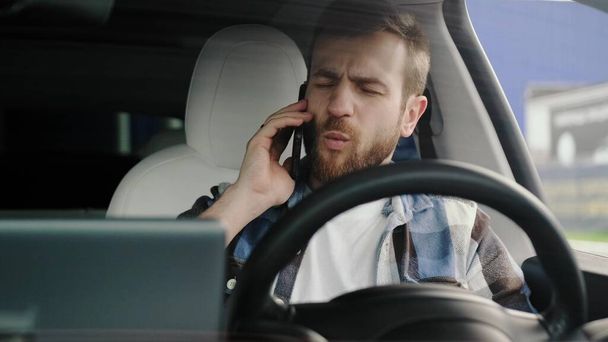 Boos man zit in de auto terwijl hij smartphone vasthoudt en praat. Lifestyle, technologie, reisconcept. Langzame beweging - Foto, afbeelding