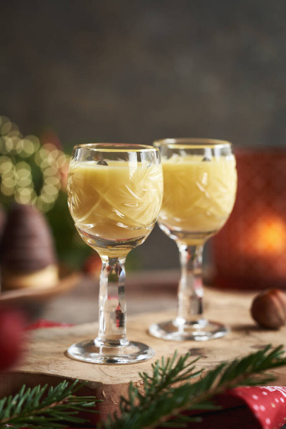 Két pohár tojáslikőr karácsonyi sütikkel és faágakkal a háttérben. - Fotó, kép