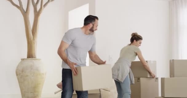 Couple, hug and living room with box in new house for real estate, mortgage and property investment. People, man and woman with embrace, happy and moving into apartment, home or relocation with smile. - Footage, Video