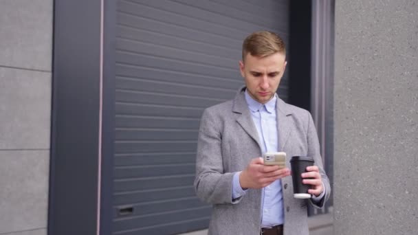 Бизнесмен держит кофе, печатает по телефону, стоит на улице. Бизнес, работа, концепция технологий. В реальном времени - Кадры, видео