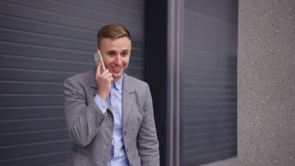 Happy young businessman standing outdoors and talking on the mobile phone, celebrating success. Business, technology concept. Real time - Footage, Video