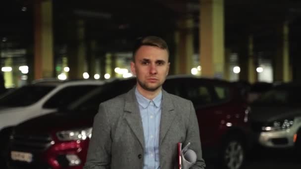 Young man in suit holding coffee and documents while walking along the parking in the evening. Business, job, people concept. Real time - Footage, Video