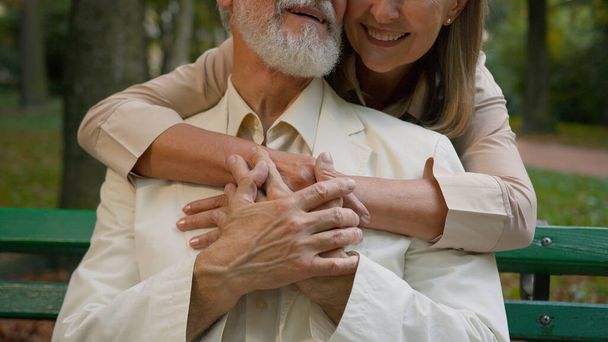 Yakın tebessüm eden beyaz bir çift mutlu bir aile, yaşlı bir kadın şehir parkının dışında yaşlı bir adama sevgiyle sarılıyor. Büyükanne ve büyükbabalar evlilik emekliliği gevşeme sağlık hizmetlerini destekliyor - Fotoğraf, Görsel
