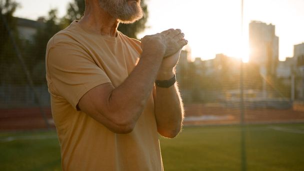 Καυκάσιος ηλικιωμένος άνδρας απλώνει τα χέρια του ζέσταμα ασκήσεις αθλητισμός συνταξιούχος πόλη σε εξωτερικούς χώρους ανατολή φύση πρωί fitness κατάρτιση υγειονομική περίθαλψη παλιό αθλητή προπόνηση αγνώριστος τρόπος ζωής δραστηριότητα - Φωτογραφία, εικόνα