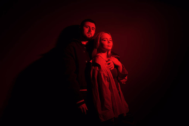 Ein junges Paar steht zusammen, eingehüllt in ein tiefrotes Licht, das eine geheimnisvolle Atmosphäre verströmt - Foto, Bild