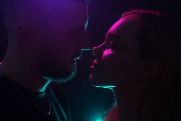 Siluetas de una pareja casi besándose, rodeada de luces de neón y sombras íntimas - Foto, Imagen