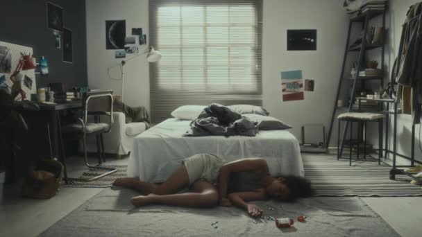Plan complet d'une adolescente inconsciente allongée sur le sol avec des pilules dispersées après s'être suicidée à la maison - Séquence, vidéo
