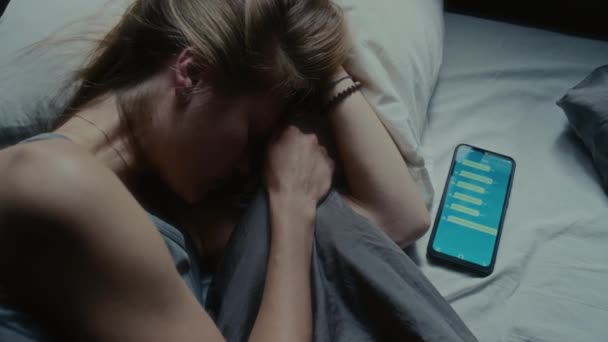Bezpośrednio nad ujęciem bezsennej dziewczyny leżącej obok niej w łóżku z telefonem komórkowym, nerwowej i zestresowanej przyczyną cyberprzemocy - Materiał filmowy, wideo