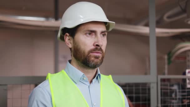 Muotokuva kasvot mies insinööri teknikko seisoo teknisessä huoneessa sähkö kytkintaulu, yllään vihreä turvaliivi, turvakypärä ympäristössä sähköaseman. Ammattitekniikka. - Materiaali, video