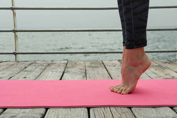 Gambe femminili su tappetino yoga su pavimento in legno all'aperto, spazio per il testo - Foto, immagini