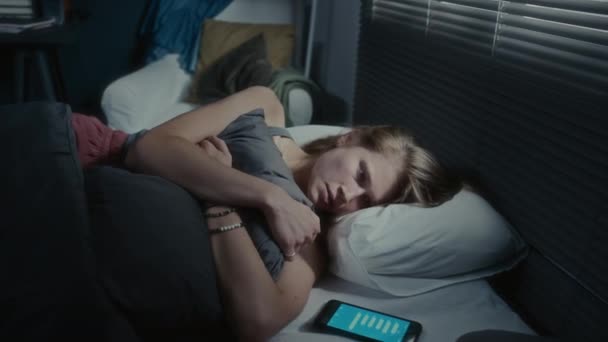 Tyttö makaa sängyssä vieressä älypuhelin tekstiviestejä näytöllä, halaus tyyny ja itku yöllä - Materiaali, video