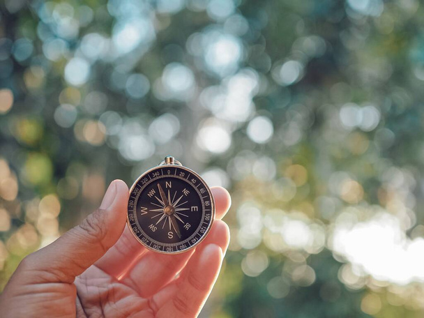 Рука держит компас с природным фоном. Концепция Всемирного дня туризма, поиск правильных направлений и путешествия - Фото, изображение