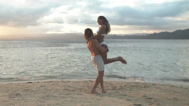 Happy couple, hug and playing at beach in relax for love, bonding or enjoying holiday vacation on ocean coast. Man carrying woman by sea water for embrace, care or outdoor romance together in nature. - Footage, Video