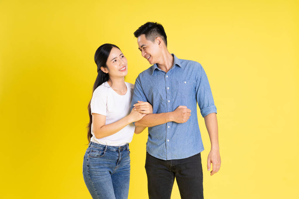 黄色の背景にポーズするアジアのカップルのイメージ - 写真・画像