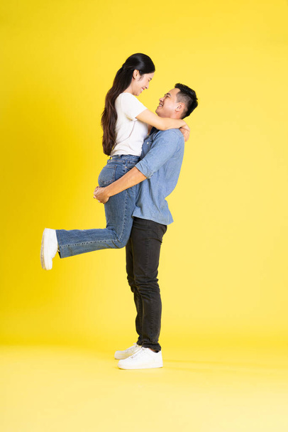 黄色の背景にポーズするアジアのカップルの完全なボディイメージ - 写真・画像