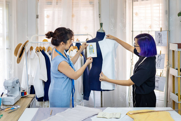 Team von modischen freiberuflichen Schneiderinnen, die Design und Stil für neue maßgeschneiderte Kleider auswählen, während sie mit Schaufensterpuppe im Atelier für Modedesign und Bekleidungsindustrie arbeiten - Foto, Bild