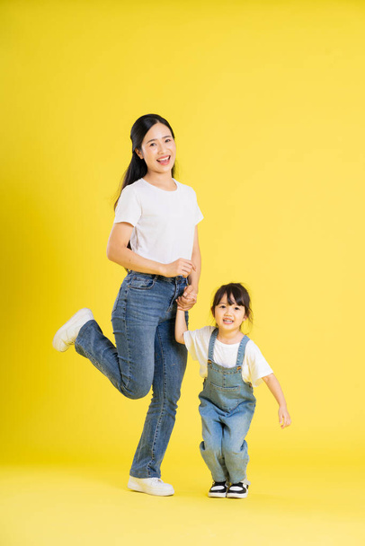 Asyalı anne ve kızının sarı arka planda poz verişi. - Fotoğraf, Görsel