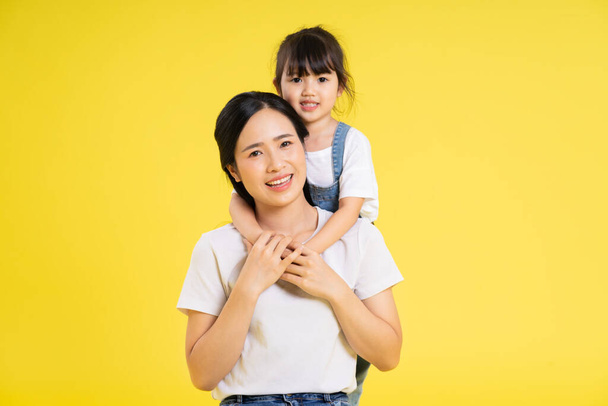 image of asian mother and daughter posing on a yellow background - Photo, Image