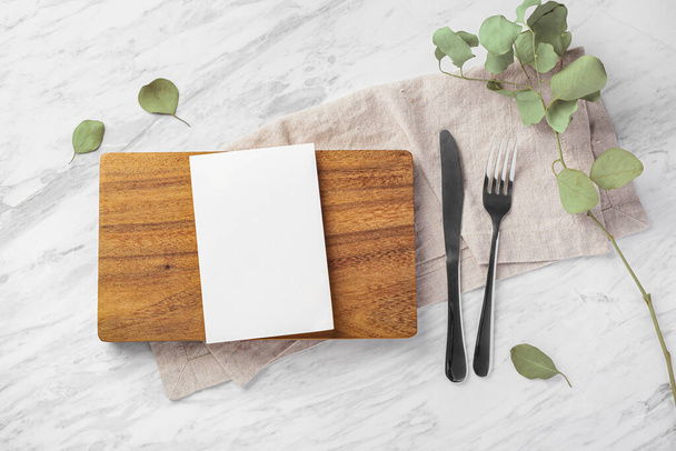 Макет деревянной доски и карты меню с вилкой и ножом на мраморном кухонном столе, вид сверху - Фото, изображение