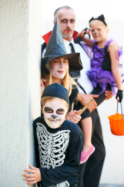 Portrait, halloween und eine Familie in Kostümen für Tricks oder behandeln Tradition oder Feiertage. Mutter, Vater und Kinder in Fantasiekleidern vor einer Tür, um sich an Heiligabend gemeinsam zu verkleiden. - Foto, Bild