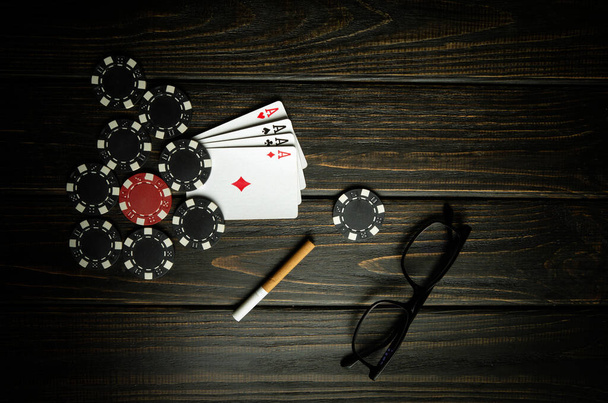 Velmi populární a hazardní hra poker s vítěznou kombinací čtyř druhů nebo čtyřkolky. Karty s hranolkami a sklenicemi s cigaretou na černém vinobraní stolu v pokerovém klubu. - Fotografie, Obrázek