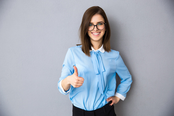 Smiling businesswoman with thumb up over gray background - Foto, Bild