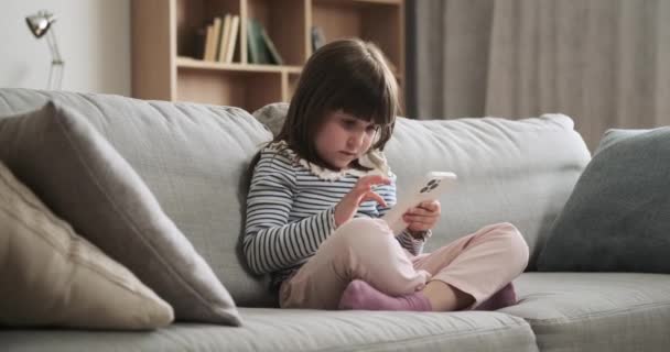 Oturma odasında, konsantre olmuş genç bir kız elinde telefonla kanepede oturuyor. Niyeti ekrana bakması derin bir konsantrasyon göstergesi. Özümsenmiş bir düşünce anı yaratıyor.. - Video, Çekim